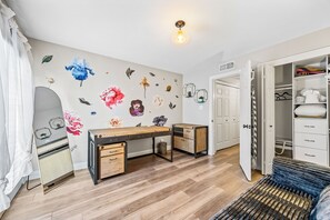 Ein Zimmer mit einem Holztisch, einem Kleiderschrank und einem Bett mit weißer Daunendecke.