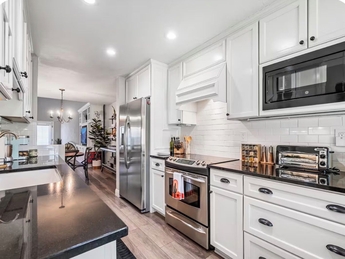 A modern kitchen with white cabinetry, stainless steel appliances, and a black countertop.