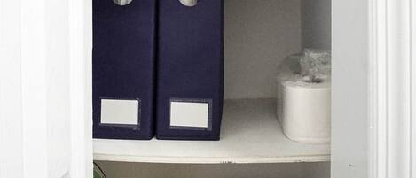 A closet with shelves containing folded towels, storage boxes, and a first aid kit.