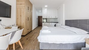 Une chambre moderne avec un grand lit, un bureau et, au fond, un coin cuisine.