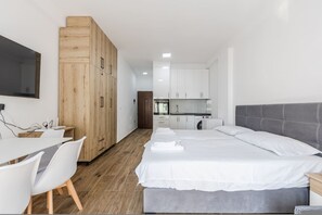 A modern bedroom with a large bed, a desk, and a kitchenette in the background. - Wave Stay Studio Durr s Waterfront (Durrës)