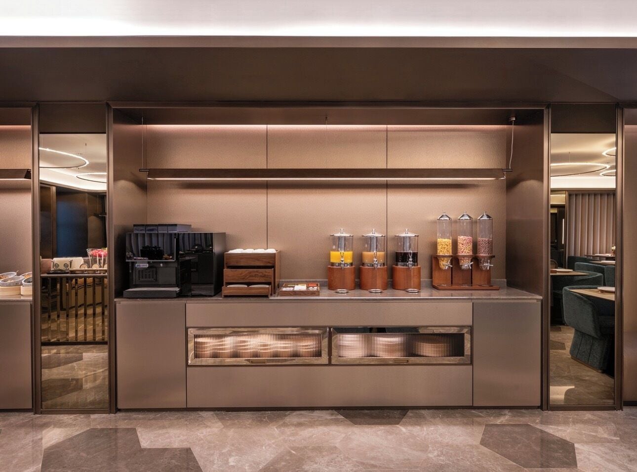 A modern hotel room with a built-in kitchenette, a coffee machine, and a breakfast bar with dispensers.