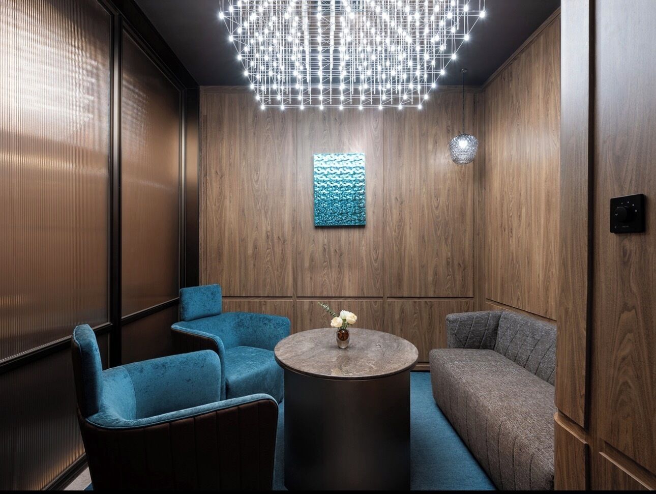 Eine moderne Lounge mit einer Holzwand, einem blauen Sofa, einem blauen Sessel und einem runden Tisch mit Blumen in einer Vase.