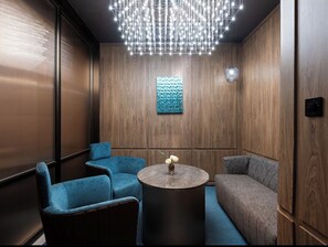 Un salon moderne avec un mur en bois, un canapé bleu, un fauteuil bleu et une table ronde agrémentée d’un vase de fleurs.