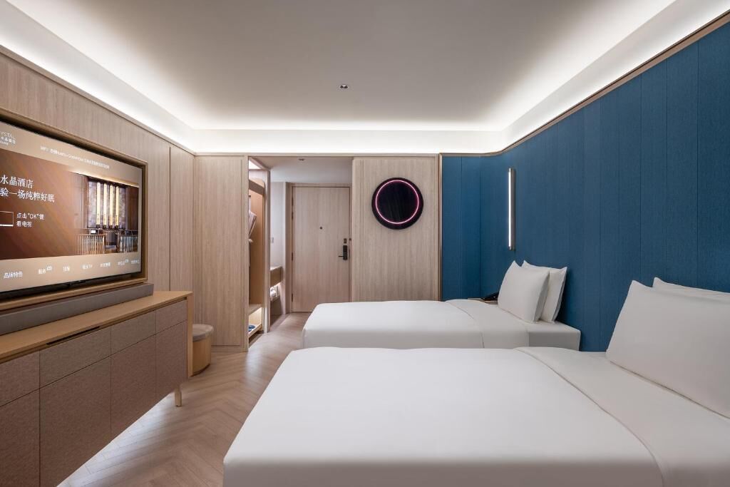 Een moderne hotelkamer met een flatscreen-televisie, twee bedden, een blauwe accentmuur en een ronde lamp.