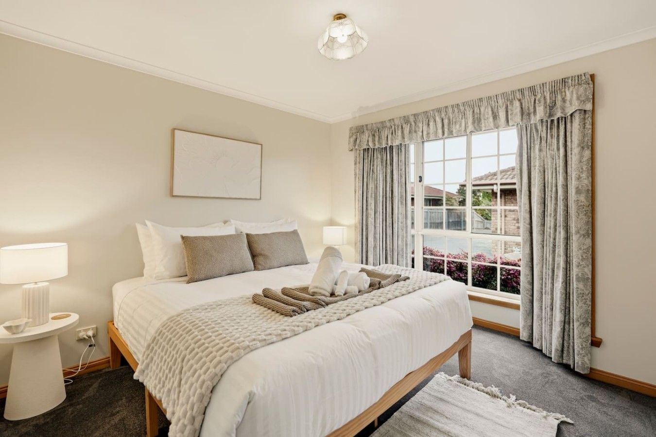 A hotel room with a large bed, bedside lamps, a window with curtains, and a view of the outside.