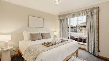 A hotel room with a large bed, bedside lamps, a window with curtains, and a view of the outside.