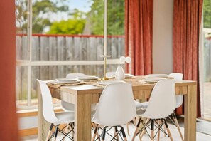 Una mesa de comedor con sillas blancas, un jarrón con flores blancas y una mesa de madera.