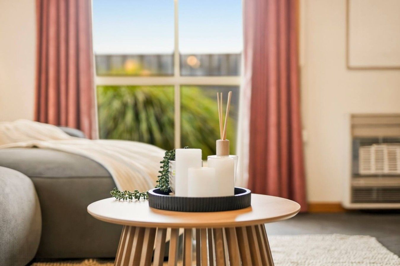 Une pièce comprenant un lit, une petite table ronde avec des bougies et des diffuseurs de parfum à bâtonnets, et une fenêtre avec des rideaux.