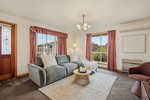 A living room with a grey sofa, a coffee table, and a view of the outdoors. - Modern 3BR Retreat | Near Launceston CBD (Youngtown)