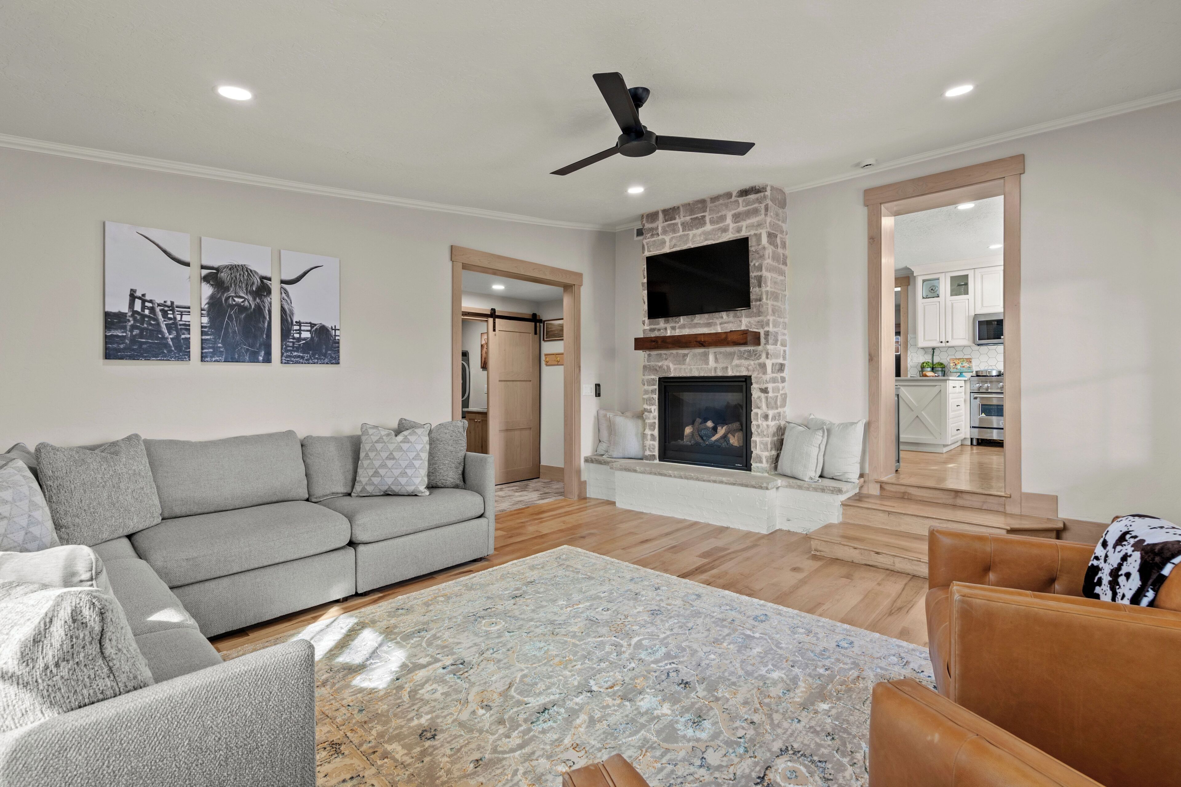 A living room with a grey sofa, a patterned rug, a fireplace, and a television mounted on a stone wall.