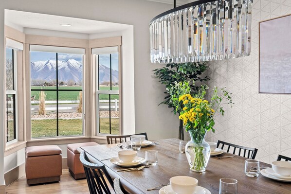 A dining area with a table set for four, a vase with yellow flowers, and a view of mountains through large windows.