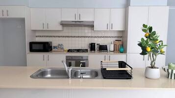 A modern kitchen with white cabinets, a stainless steel sink, a microwave, a stove, and a potted lemon tree.
