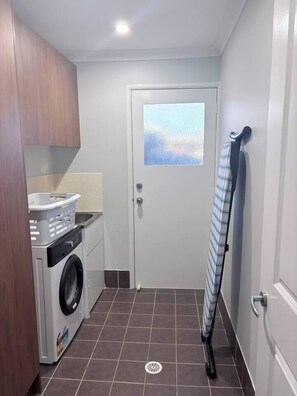 A compact laundry area with a washing machine, a drying rack, and a door with a frosted glass window. - The Laguna Residence by Esteem Retreats (Kellyville Ridge)