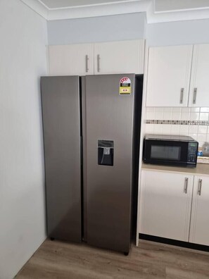 A kitchen with a stainless steel refrigerator and a microwave on the countertop. - The Laguna Residence by Esteem Retreats (Kellyville Ridge)