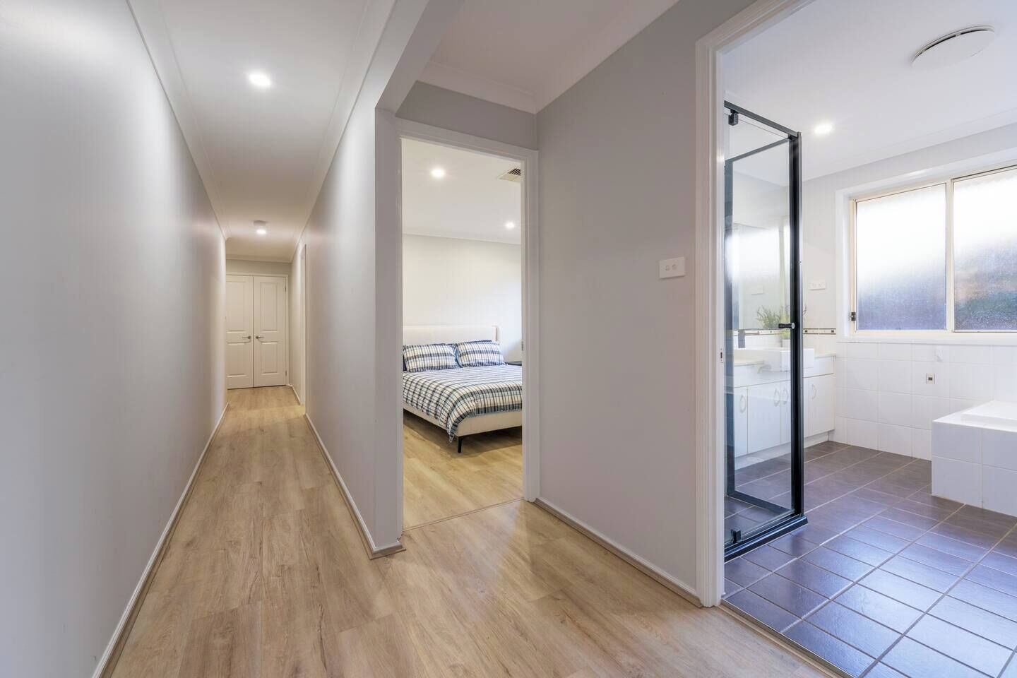 A hallway leading to a bedroom with a bed and a bathroom with a bathtub.