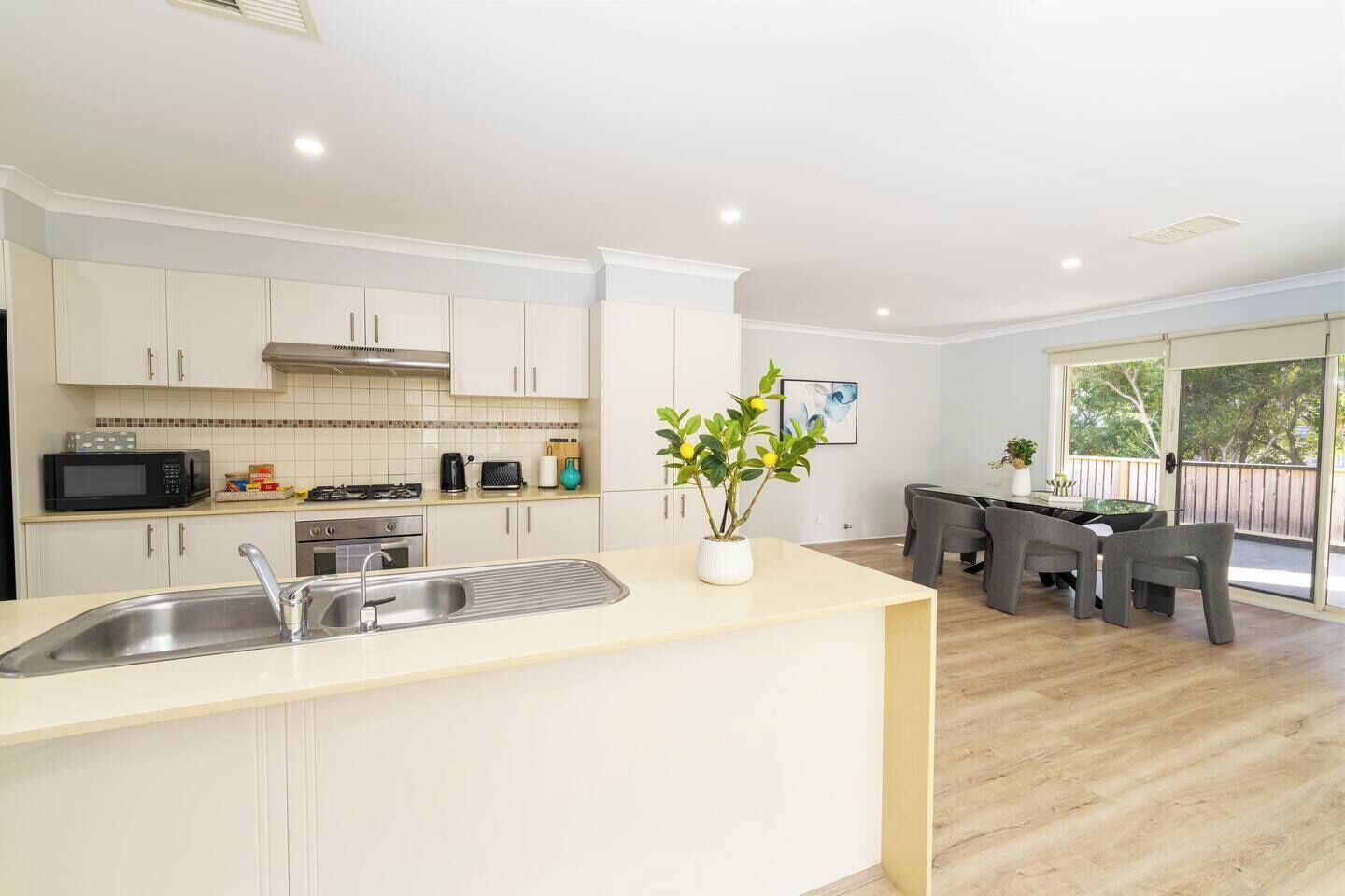A modern kitchen with white cabinets, a stainless steel sink, and a dining area with a table and chairs.