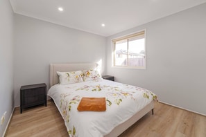 Un dormitorio con cama, mesita de noche, ventana y radiador.