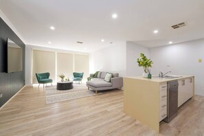 Una sala moderna con un sofá, dos sillones, una mesa de centro y una cocina con fregadero y lavavajillas.