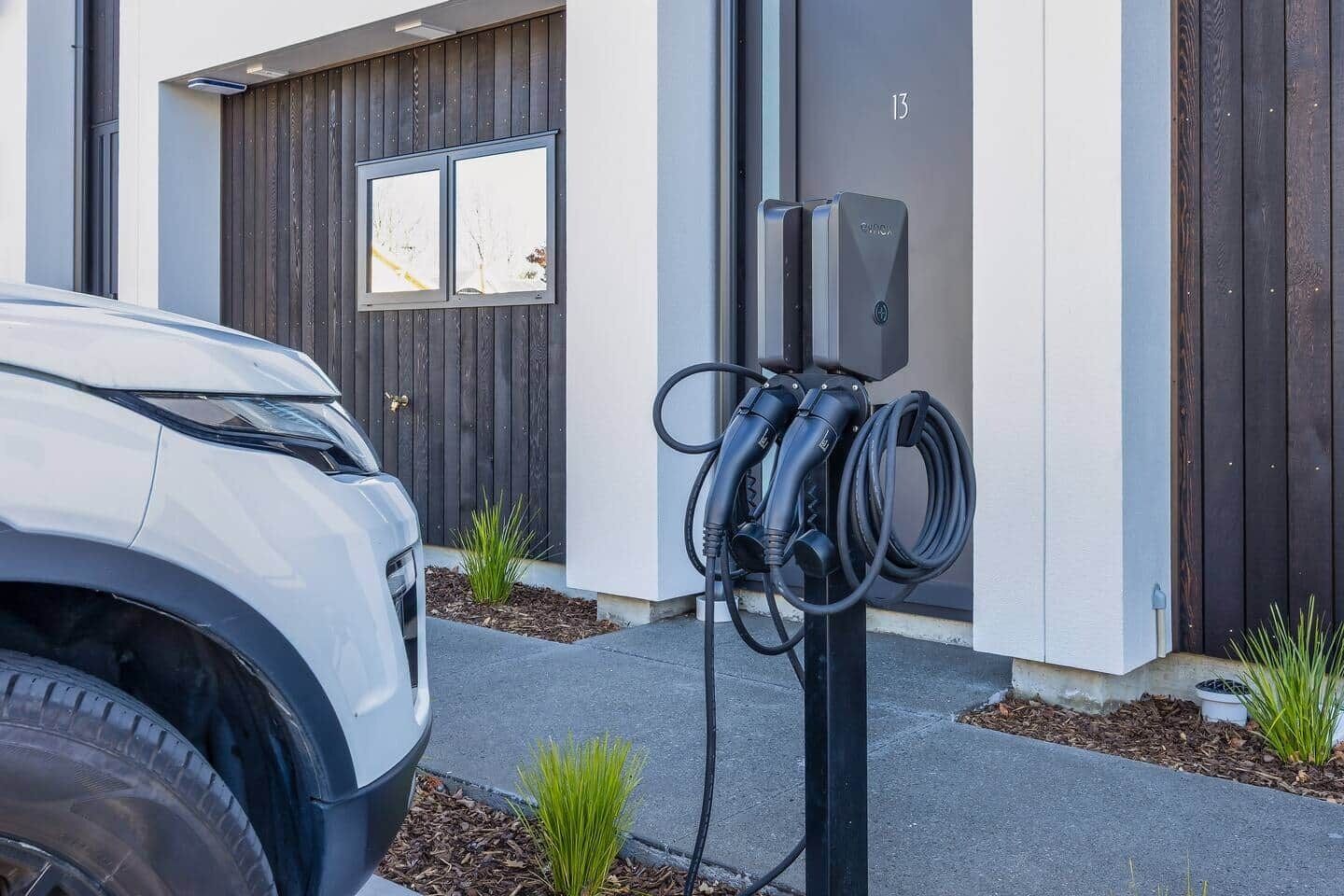 A modern building with a white facade, a dark wooden door, and a parking area with a white car and electric vehicle charging station.