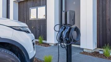 A modern building with a white facade, a dark wooden door, and a parking area with a white car and electric vehicle charging station.