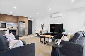 A modern living room with a sofa, a coffee table, and a flat-screen TV. - Luxury on Gloucester (Christchurch)
