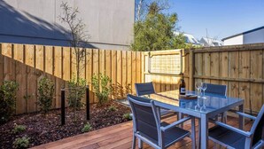 A patio with a table and chairs, a wooden fence, and a small garden area. - Luxury on Gloucester (Christchurch)