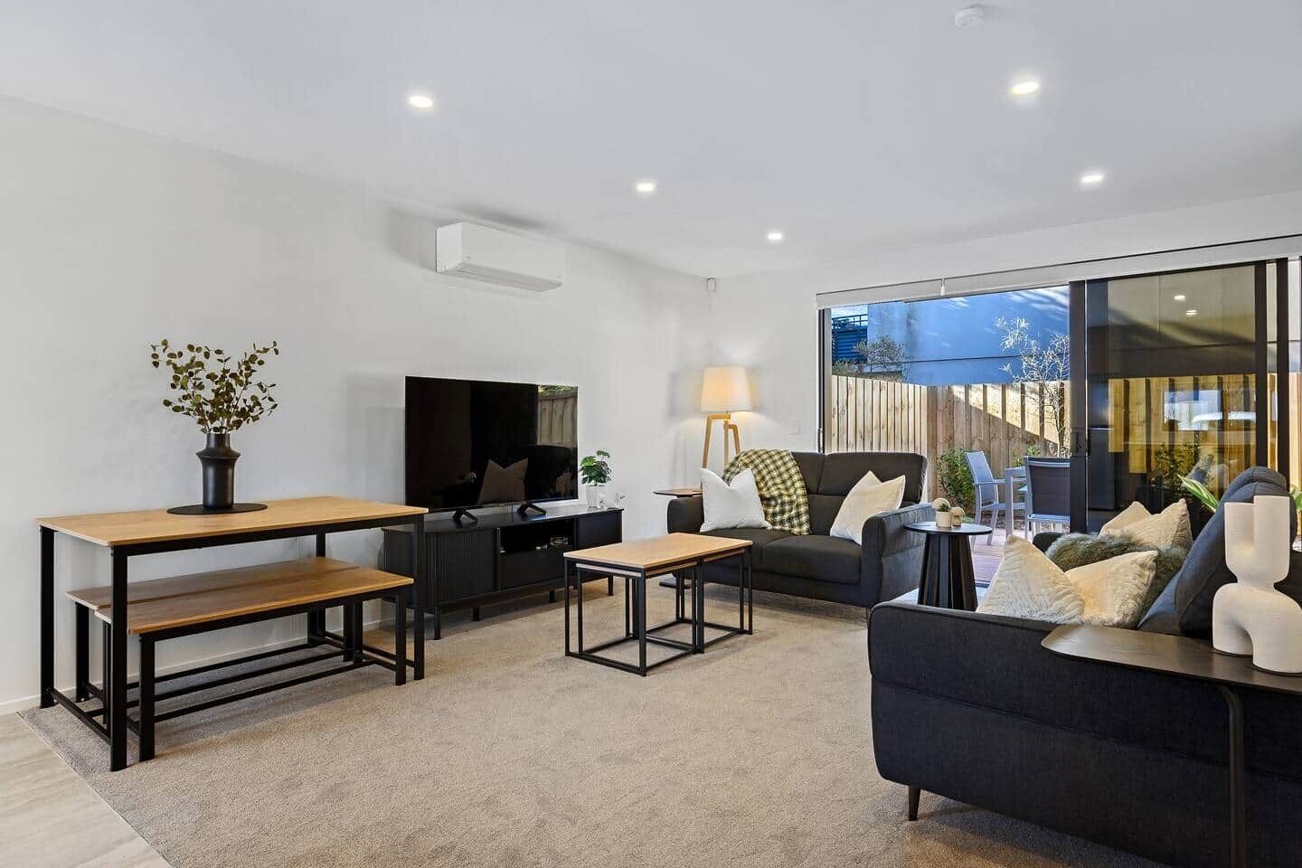 A modern living room with a flat-screen TV, a sofa, a coffee table, and a dining table.