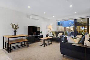 A modern living room with a flat-screen TV, a sofa, a coffee table, and a dining table. - Luxury on Gloucester (Christchurch)