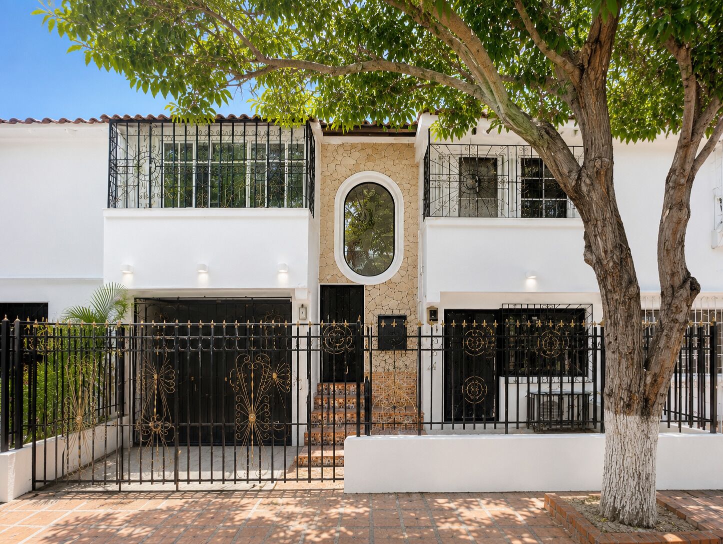 Un edificio de dos pisos con fachada blanca, pared de piedra y reja de metal negro.