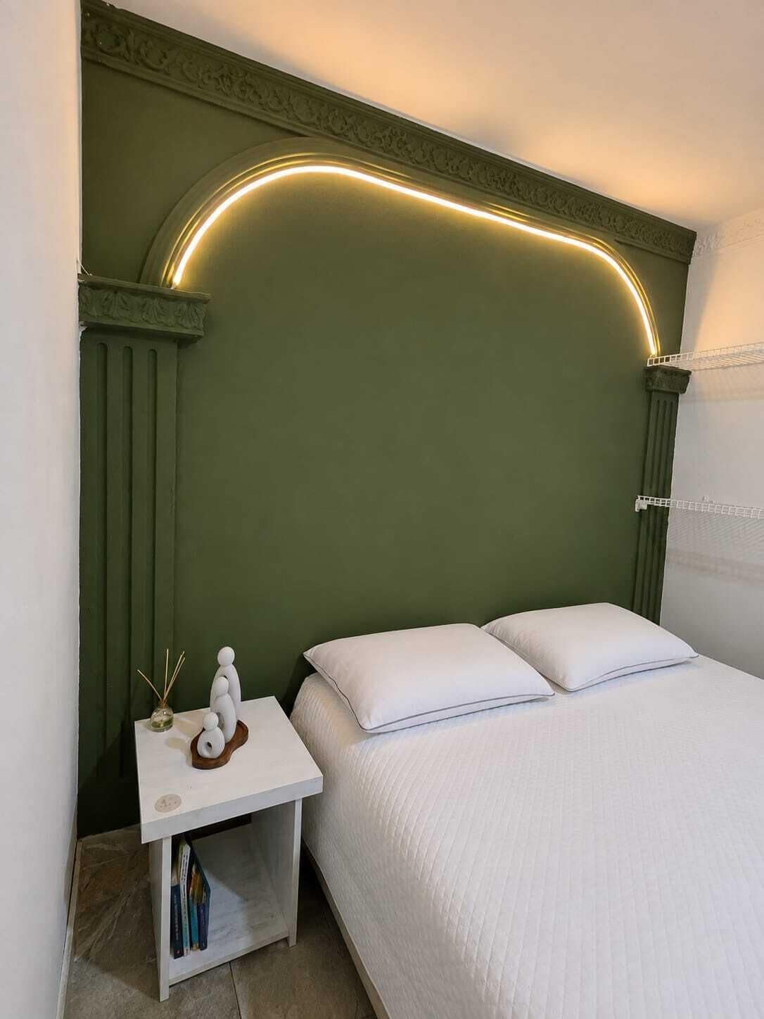 Ein Schlafzimmer mit einem grünen Kopfteil, weißer Bettwäsche und einem Nachttisch mit einem Buch und Dekoration.