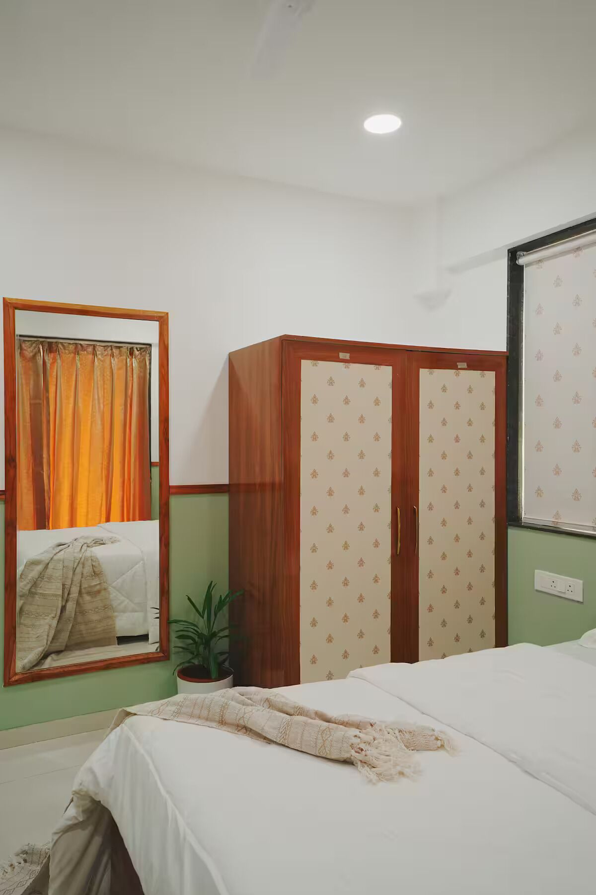 A bedroom with a bed, a wardrobe, a mirror, and a potted plant.