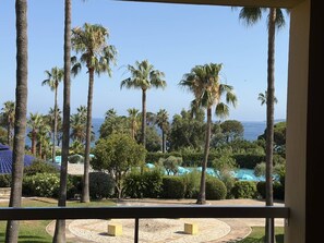 A view from a balcony overlooking a pool area with palm trees and a clear sky. - 2-Bedroom Apartment in Les Rivages des Issambres (LES ISSAMBRES)