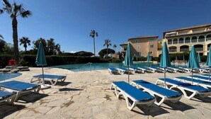 A poolside area with lounge chairs and umbrellas, a stone pathway, and a building in the background. - 2-Bedroom Apartment in Les Rivages des Issambres (LES ISSAMBRES)