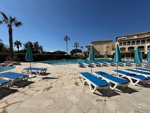 A poolside area with lounge chairs and umbrellas, a stone pathway, and a building in the background. - 2-Bedroom Apartment in Les Rivages des Issambres (LES ISSAMBRES)