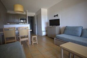 A compact living space with a kitchenette, a sofa, a TV, and a dining area with chairs. - 2-Bedroom Apartment in Les Rivages des Issambres (LES ISSAMBRES)