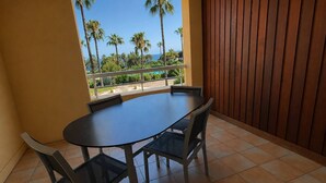 A balcony with a round table and chairs, a view of palm trees and a body of water. - 2-Bedroom Apartment in Les Rivages des Issambres (LES ISSAMBRES)