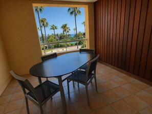 A balcony with a round table and chairs, a view of palm trees and a body of water. - 2-Bedroom Apartment in Les Rivages des Issambres (LES ISSAMBRES)