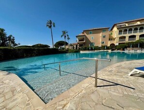 A swimming pool with a metal railing, surrounded by stone tiles and palm trees. - 2-Bedroom Apartment in Les Rivages des Issambres (LES ISSAMBRES)