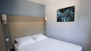 A hotel room with a bed, a headboard, two wall-mounted lamps, and a painting on the wall. - 2-Bedroom Apartment in Les Rivages des Issambres (LES ISSAMBRES)