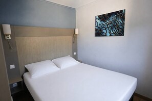 A hotel room with a bed, a headboard, two wall-mounted lamps, and a painting on the wall. - 2-Bedroom Apartment in Les Rivages des Issambres (LES ISSAMBRES)