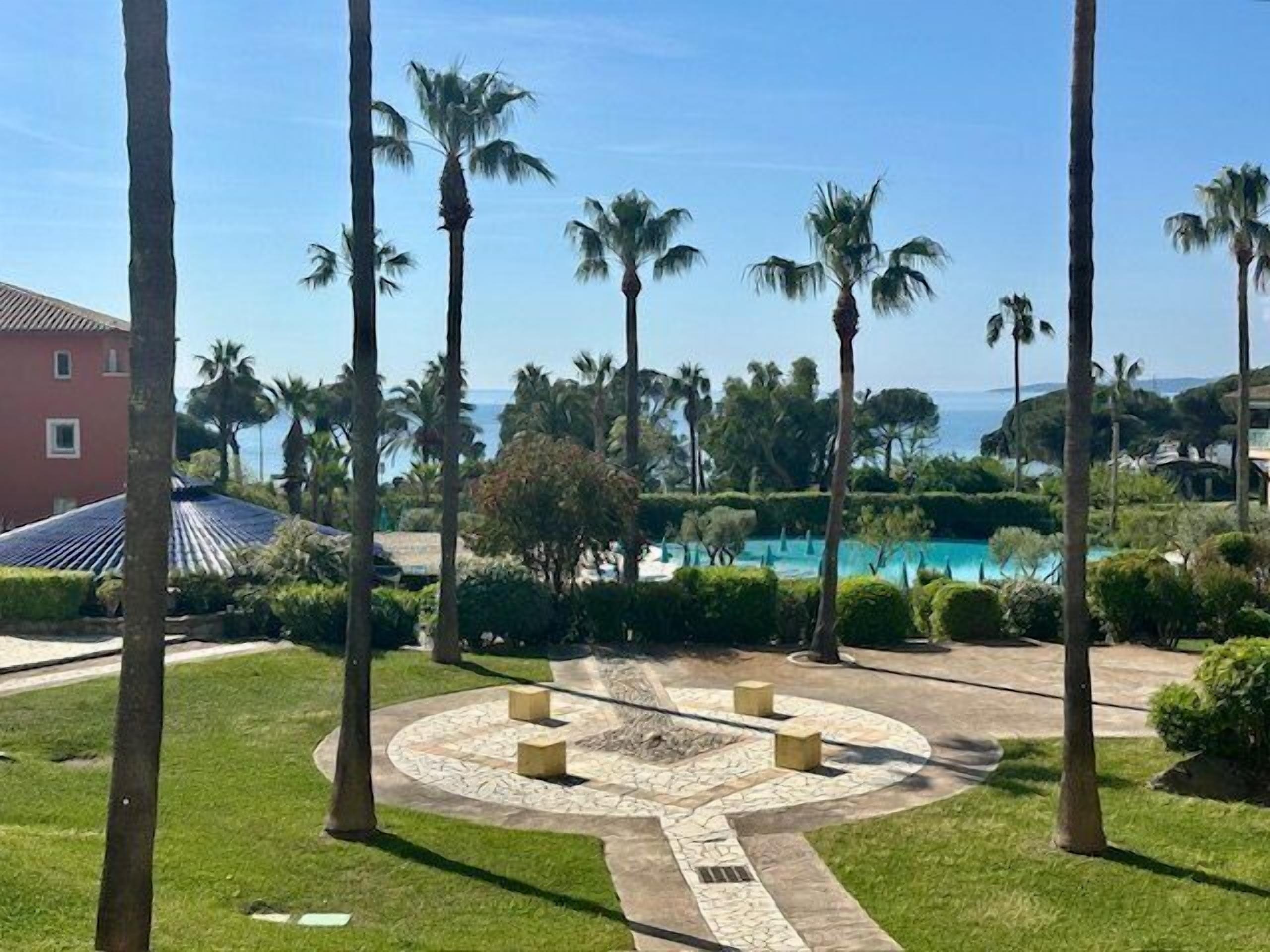 A pool area with palm trees, a circular stone pattern, and a building in the background.
