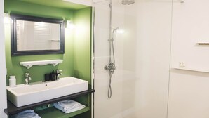 Casa de banho com lavatório branco, espelho e cabine de duche com parede de vidro.