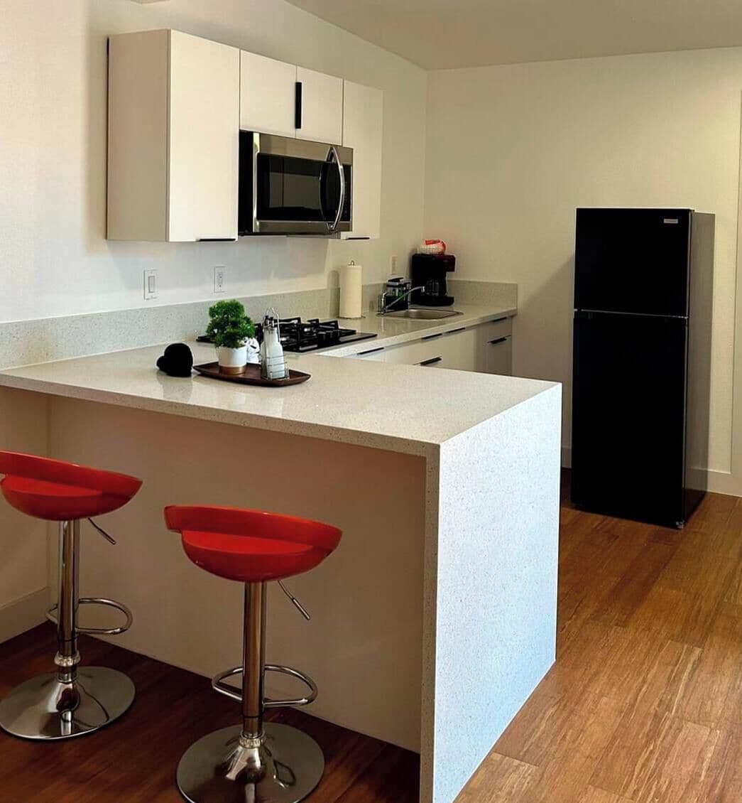 A modern kitchen with a white countertop, stainless steel appliances, and red bar stools.