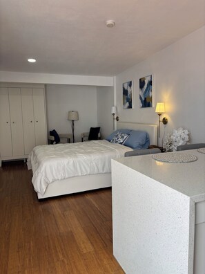 Ein Hotelzimmer mit Bett, Nachttisch, Lampe, Kunstwerk und einem Schrank.