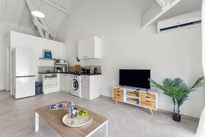 Eine moderne Küche mit integriertem Mikrowellenherd, Backofen und Waschmaschine. Ein Flachbildfernseher steht auf einem Holzschrank und ein Blumentopf ist ebenfalls vorhanden.