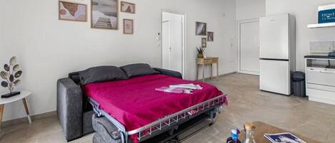A bedroom with a bed, a small table with a tray of items, and a kitchenette area.