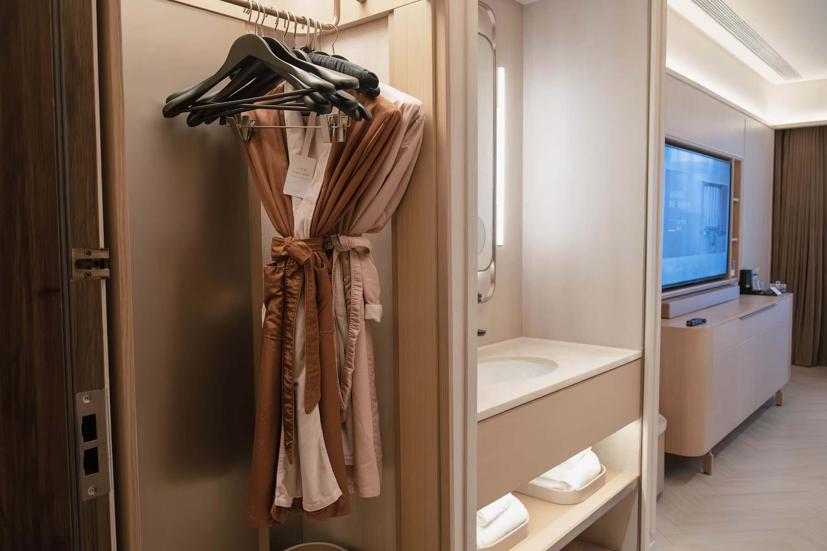 A hotel bathroom with a robe hanging on a rack, a sink, and a mirror.