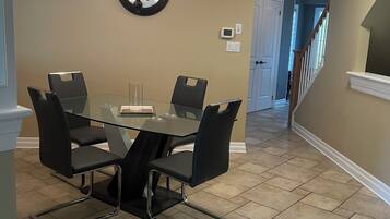 A dining area with a glass table and chairs, a chandelier, and a staircase leading to another room.