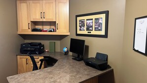Ein kleiner Büroraum mit Schreibtisch, Computer, Drucker und einem gerahmten Bild an der Wand.